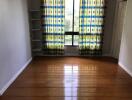 Empty room with hardwood flooring, window with patterned curtains, and built-in shelving