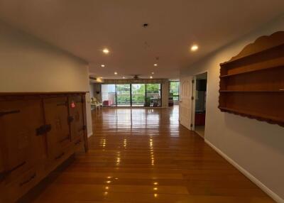 spacious living area with wooden flooring, built-in shelves, large windows, and balcony access