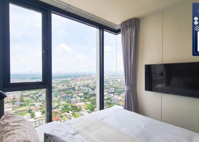 Bedroom with a large window offering a panoramic city view, wall-mounted TV, and queen-sized bed