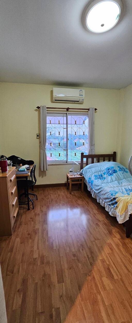 Bedroom with wooden floor, single bed, desk, and window with curtains.