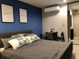 A cozy bedroom with blue accent wall, air conditioner, and workspace