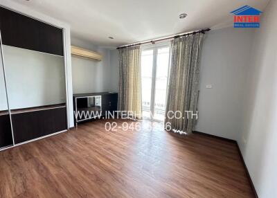 Spacious bedroom with wooden flooring, built-in wardrobe, air conditioning, and large window with curtains