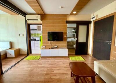 Modern living room with wooden floor, TV, and adjacent kitchen