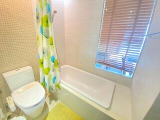 Modern bathroom with bathtub, toilet, and window with blinds