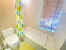 Modern bathroom with bathtub, toilet, and window with blinds