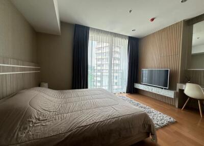 Spacious bedroom with a large window, modern TV setup, and wooden flooring