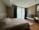 Spacious bedroom with a large window, modern TV setup, and wooden flooring