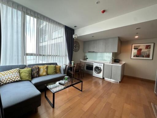 Modern living space with a kitchen area, featuring a sectional sofa and a washing machine