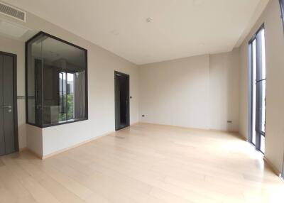 A spacious empty bedroom with large windows, light wooden flooring, and a glass-enclosed shower area.