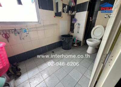 Bathroom with tiled floors and walls, toilet, and some cleaning supplies