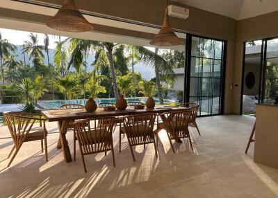 Spacious dining area with wooden furniture and large windows overlooking a pool