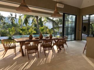 Spacious dining area with wooden furniture and large windows overlooking a pool