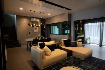 Stylish modern living room with a sectional sofa, dining area, glass table, and contemporary lighting