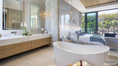 Spacious and luxurious bedroom with an open bathroom featuring a modern freestanding bathtub, large vanity with dual sinks, and large windows overlooking a lush garden.