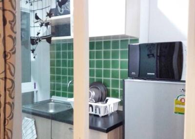Compact kitchen area with green tiled backsplash, sink, microwave, and fridge