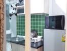 Compact kitchen area with green tiled backsplash, sink, microwave, and fridge