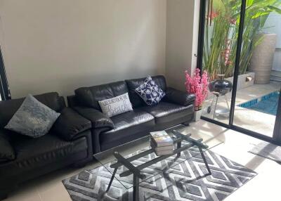 Modern living room with black leather sofas, glass coffee table, and sliding glass door leading to outdoor pool