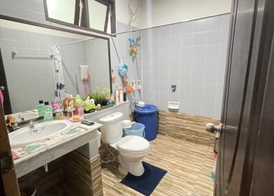 Modern bathroom with tiled walls and floor, featuring a large mirror, sink, toilet, and various toiletries