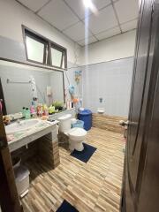 Modern bathroom with tiled walls and floor, featuring a large mirror, sink, toilet, and various toiletries