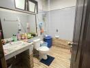 Modern bathroom with tiled walls and floor, featuring a large mirror, sink, toilet, and various toiletries