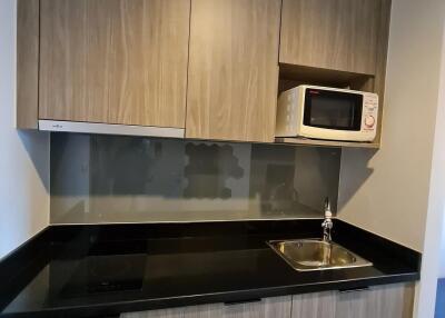 Small kitchen with wooden cabinets, black countertop, and built-in microwave