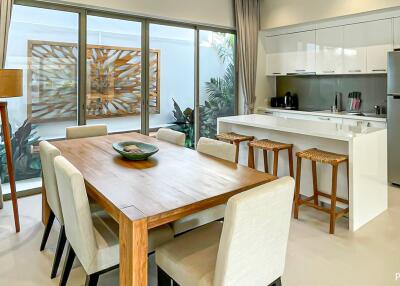 Modern kitchen and dining area with wooden dining table, bar stools, and large windows
