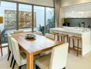 Modern kitchen and dining area with wooden dining table, bar stools, and large windows