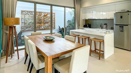 Modern kitchen and dining area with wooden dining table, bar stools, and large windows