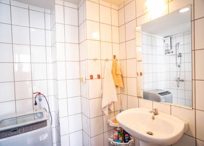 A bathroom with white tiled walls, a sink, mirror, and washing machine.