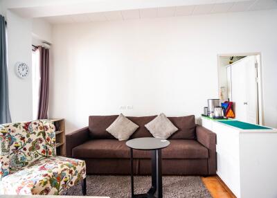 Modern living room with a brown sofa, patterned chair, and small kitchenette