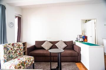 Modern living room with a brown sofa, patterned chair, and small kitchenette