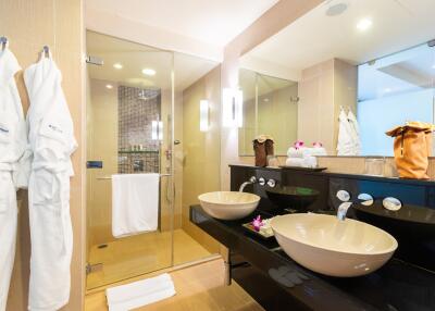 Modern bathroom with double sinks, glass shower, and bathrobes