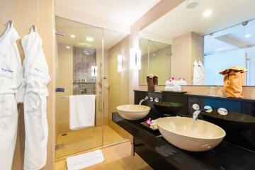 Modern bathroom with double sinks, glass shower, and bathrobes