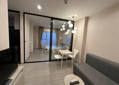 Modern living room with grey sofa, dining table, and view into bedroom