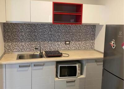 Modern kitchen with minimalist design featuring a mosaic backsplash, stainless steel sink, microwave, and refrigerator.
