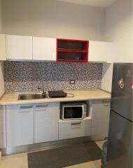 Modern kitchen with minimalist design featuring a mosaic backsplash, stainless steel sink, microwave, and refrigerator.