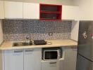 Modern kitchen with minimalist design featuring a mosaic backsplash, stainless steel sink, microwave, and refrigerator.