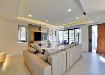 Modern living room with beige sectional sofa, wall-mounted TV, recessed lighting, and large windows