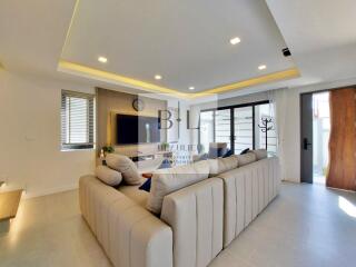 Modern living room with beige sectional sofa, wall-mounted TV, recessed lighting, and large windows