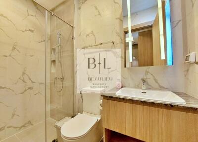 Modern bathroom with marble tiles, glass shower, toilet, and sink with wooden cabinet