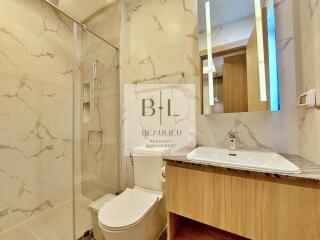 Modern bathroom with marble tiles, glass shower, toilet, and sink with wooden cabinet