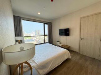 Bedroom with a view, featuring a bed, wall-mounted TV, a nightstand, and a large window