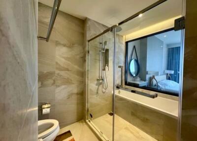 Modern bathroom with marble tiles, glass shower enclosure, and view into the bedroom