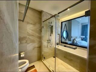 Modern bathroom with marble tiles, glass shower enclosure, and view into the bedroom