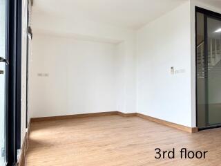 Empty room with wooden flooring and a staircase visible through a glass door