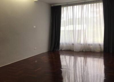 Empty living room with dark wood flooring and large window with curtains