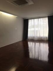 Empty living room with dark wood flooring and large window with curtains