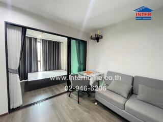 Living room with gray sofa, small table, and sliding glass door leading to bedroom