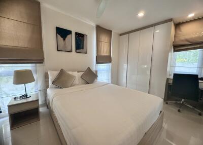 Modern bedroom with double bed, white wardrobe, bedside table with lamp, desk, and chair.