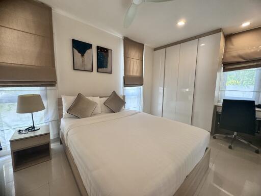 Modern bedroom with double bed, white wardrobe, bedside table with lamp, desk, and chair.